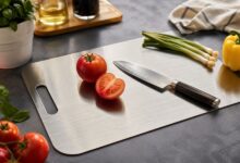 Titanium cutting board on a kitchen counter with vegetables and a chef knife